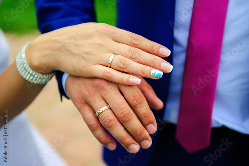 Hands of the newlyweds close-up. Gold wedding rings on the finger of bride and groom, wedding manicure. Concept of a wedding celebration.
