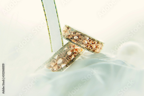 Vintage wedding rings among white ribbons, close-up. Gold rings with patterns on a blurred white background. Wedding and family traditions.
