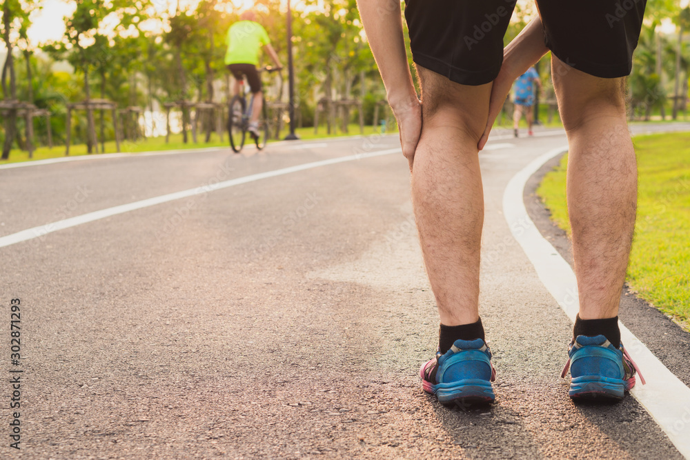 Knee Injuries. Young sport man holding knee with his hands in pain after suffering muscle injury during a running workout at park. Healthcare and sport concept. Knee Injuries. Young sport man holding knee with his hands in pain after suffering muscle injury during a running workout at park. Healthcare and sport concept.
