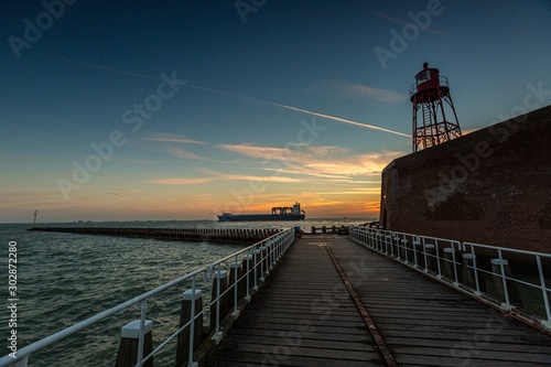 Low angle shot of a pier leading to the ocean during sunset in Vlissingen, Zeeland, Netherlands photo