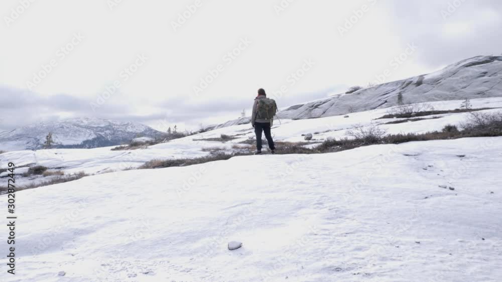 Backpacker looks over the scenic winter landscape and is approached from behind Backpacker looks over the scenic winter landscape and is approached from behind