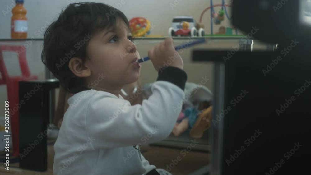 Toddler young boy sits in front of the TV and chews on a pencil eraser Toddler young boy sits in front of the TV and chews on a pencil eraser