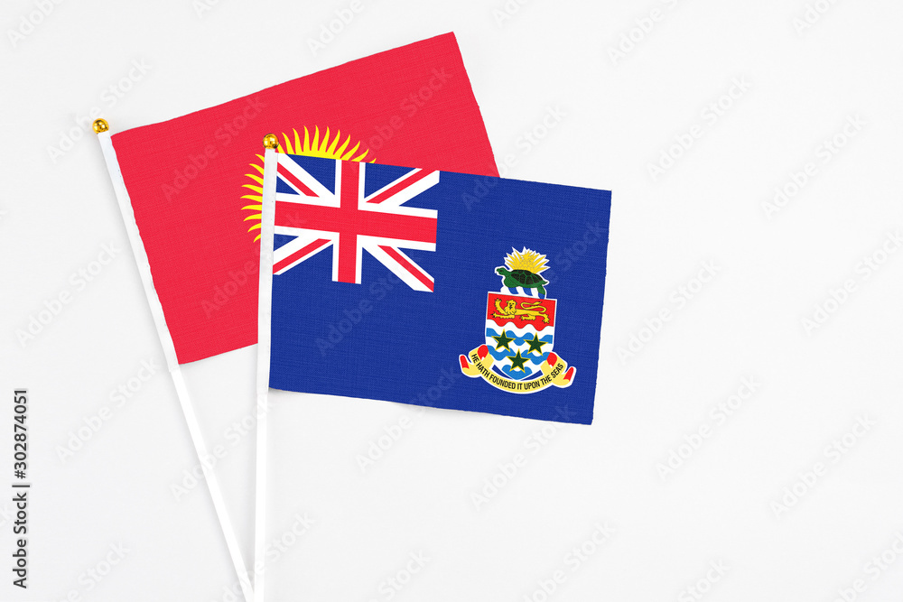 Fototapeta premium Cayman Islands and Kyrgyzstan stick flags on white background. High quality fabric, miniature national flag. Peaceful global concept.White floor for copy space.