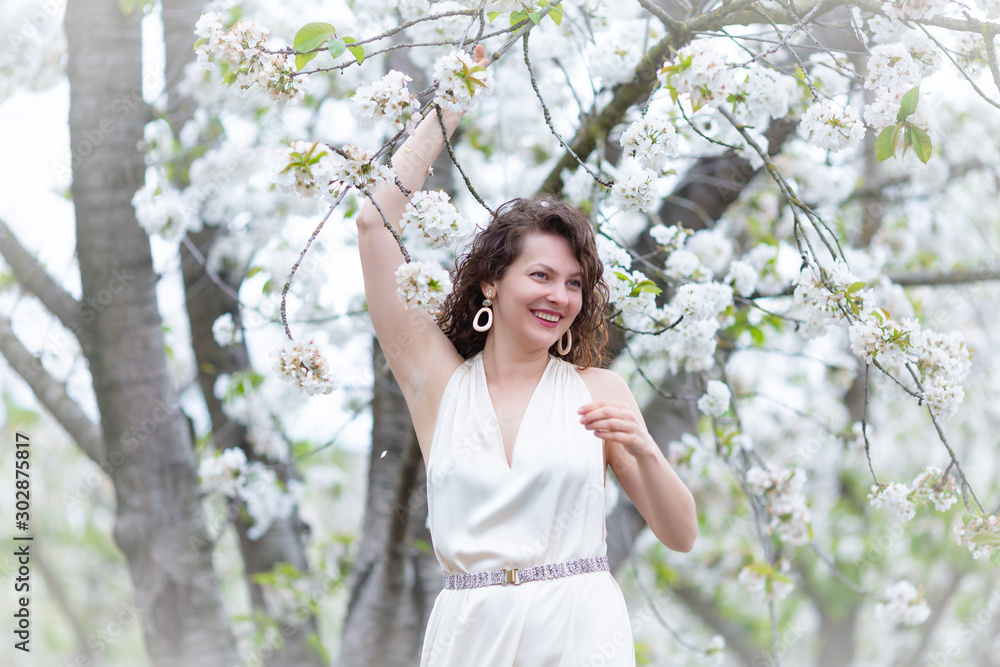 A portrait of beautiful young Caucasian woman with curly dark hair in blossoming orchard A portrait of beautiful young Caucasian woman with curly dark hair in blossoming orchard