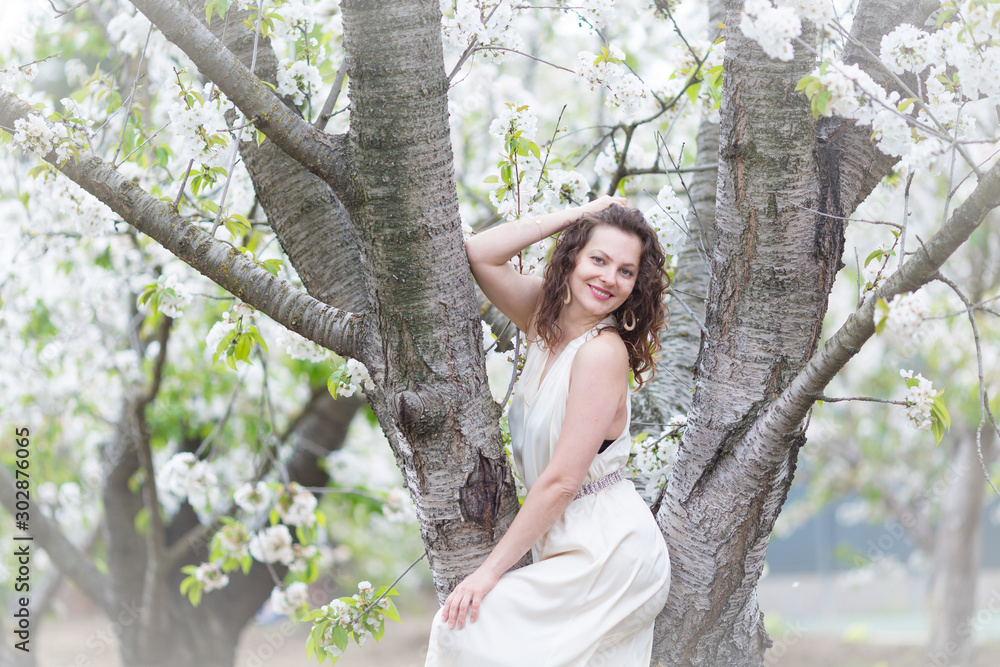 A portrait of beautiful young Caucasian woman with curly dark hair in blossoming orchard A portrait of beautiful young Caucasian woman with curly dark hair in blossoming orchard