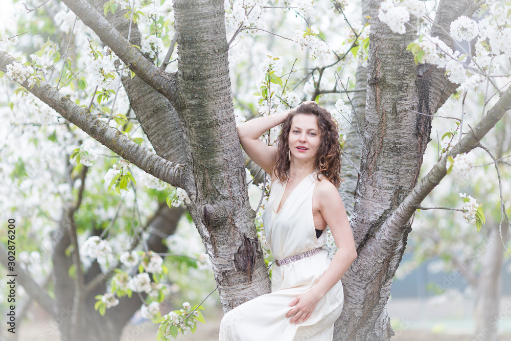 A portrait of beautiful young Caucasian woman with curly dark hair in blossoming orchard A portrait of beautiful young Caucasian woman with curly dark hair in blossoming orchard