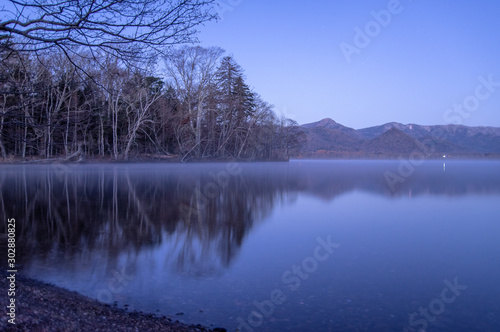薄明の湖岸。静水に映る風景。屈斜路湖、北海道、日本。
