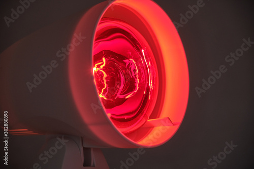 Close up of infrared lamp glowing in the dark with its warming red light to cure for example colds or tensions. photo