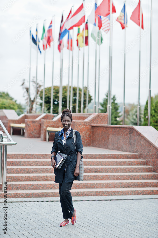 African student female posed with backpack and school items on yard of university, against flags of different countries. African student female posed with backpack and school items on yard of university, against flags of different countries.