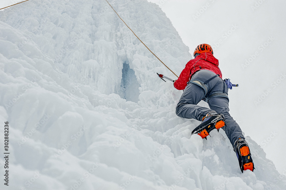 Alpinist woman with ice tools axe in orange helmet climbing a l Alpinist woman with ice tools axe in orange helmet climbing a l
