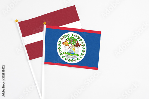 Belize and Latvia stick flags on white background. High quality fabric, miniature national flag. Peaceful global concept.White floor for copy space.