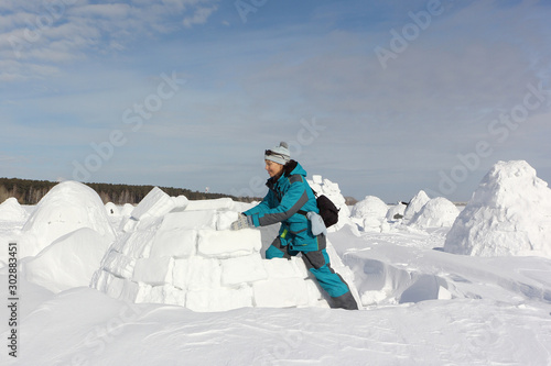 Happy woman in warm clothes building an igloo on a snow glade in the winter,  Novosibirsk, Russia