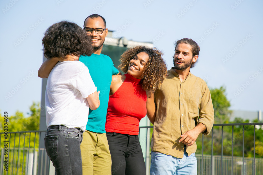 Young friends embracing and walking outdoors. Happy multiethnic friends walking and talking together on street. Friendship concept