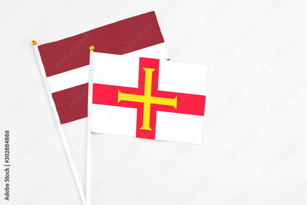 Guernsey and Latvia stick flags on white background. High quality fabric, miniature national flag. Peaceful global concept.White floor for copy space.