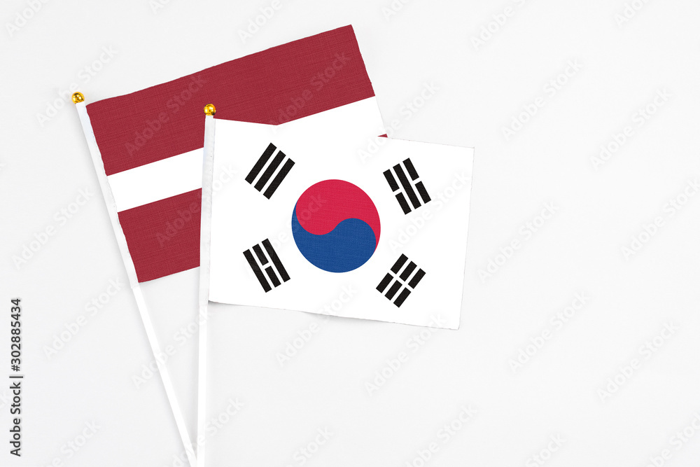 South Korea and Latvia stick flags on white background. High quality fabric, miniature national flag. Peaceful global concept.White floor for copy space.