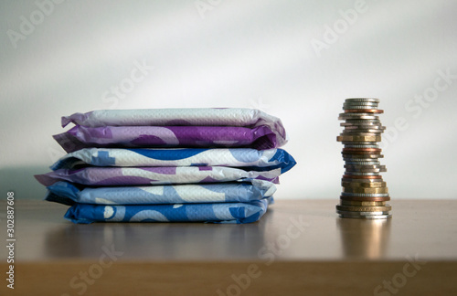 A stack of sanitary towels next to a taller stack of coins. Illustrating period poverty and unaffordability of sanitary materials for many women worldwide.