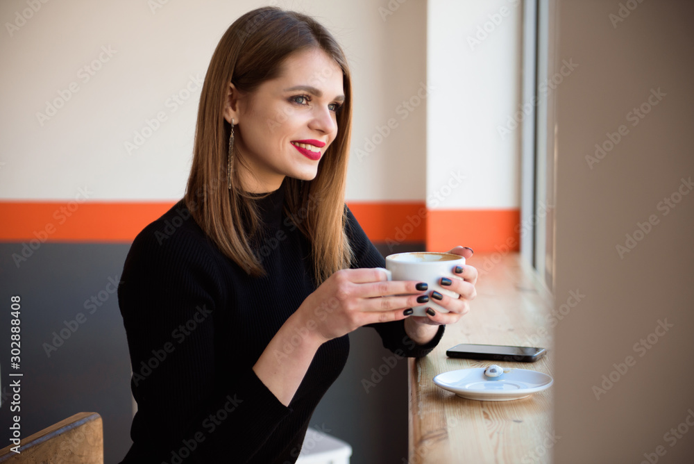 Cheerful young woman drinking warm coffee enjoying it while sitting in cafe. Attractive woman holding a cup of coffee. Cheerful young woman drinking warm coffee enjoying it while sitting in cafe. Attractive woman holding a cup of coffee.