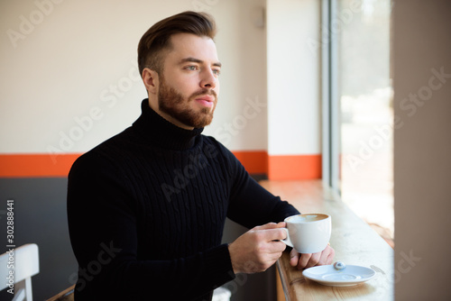 Attractive successful young businessman drinking coffee sitting at cafe table.