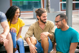 Content young friends talking on street. Cheerful young multiethnic friends sitting on wooden surface, talking and laughing. Communication concept