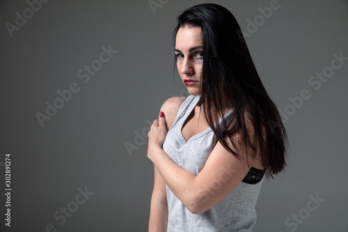 Woman in fear of domestic abuse and violence, concept of female rights. Caucasian brunette woman on grey background looks upset, sad, depressed being victim of man or husband. Has bruises, hematomas. photo