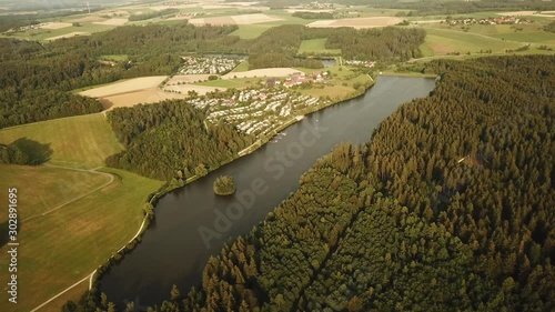 Aerial tracking shot of countryside with lake and camp site photo