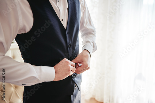 Man in white shirt buttoning waistcoat in room indoors, close up. Businessman dressing up. Fashion, style, lifestyle concept