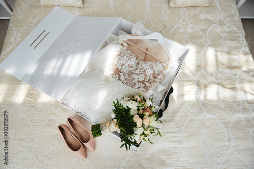 Cuadro en lienzo Luxury wedding dress in white box, beige women's shoes and bridal bouquet on bed, copy space