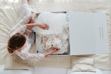 Portrait of beautiful bride in dressing gown holding luxury wedding dress on bed, copy space. Wedding concept. Top view, above