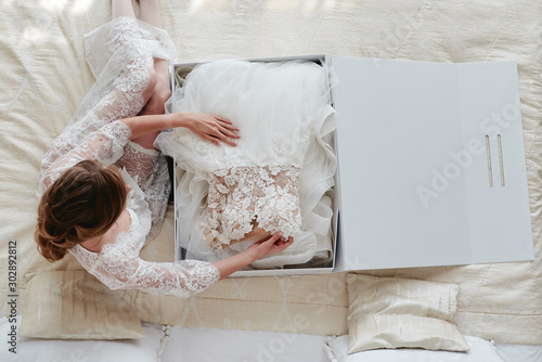Fotobehang Portrait of beautiful bride in dressing gown holding luxury wedding dress on bed, copy space