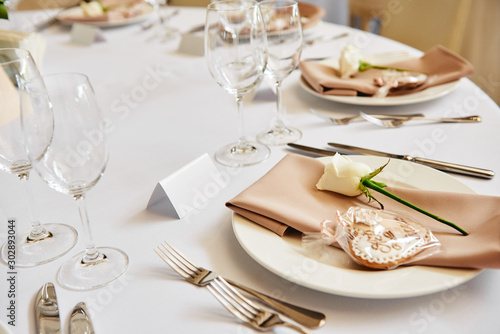 Table setting with blank guest card, white plate with beige serviette, rose, heart and cutlery on table, copy space. Place setting at wedding reception. Table served for wedding banquet in restaurant