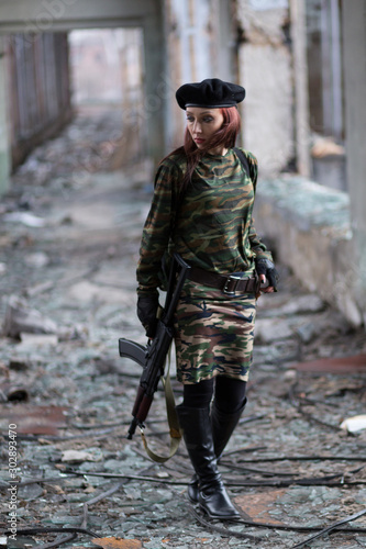 Girl in military uniform with a firearm in an abandoned building. Girl in green camouflage clothes with a Russian machine gun.