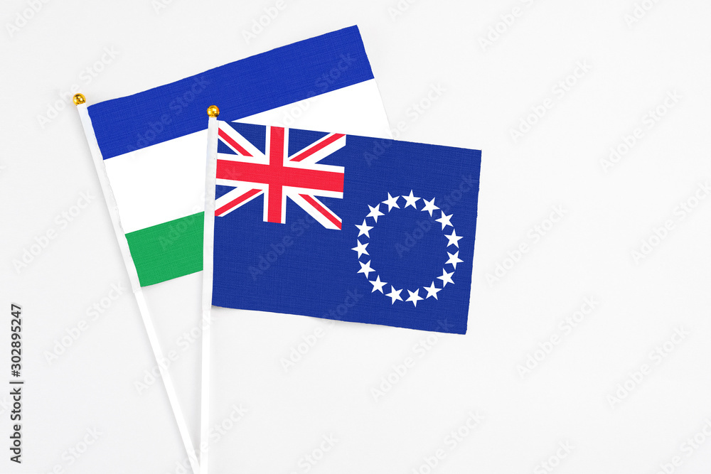Fototapeta premium Cook Islands and Lesotho stick flags on white background. High quality fabric, miniature national flag. Peaceful global concept.White floor for copy space.