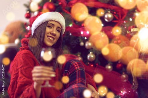 Woman with red wine, xmas tree..Happy young girl toasting with red wine