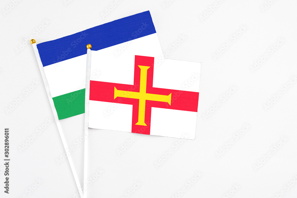 Guernsey and Lesotho stick flags on white background. High quality fabric, miniature national flag. Peaceful global concept.White floor for copy space.