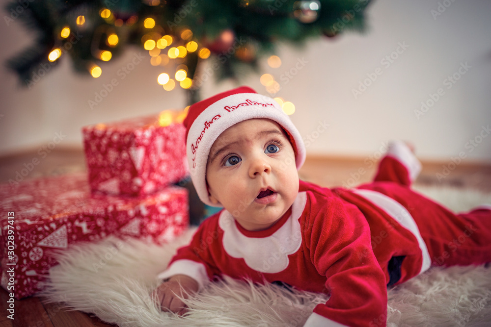 Cute baby in Christmas costume and gift box on floor at home Cute baby in Christmas costume and gift box on floor at home
