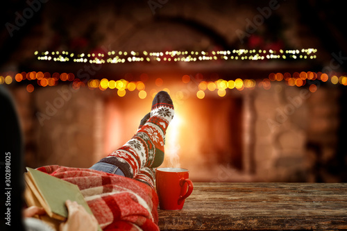 Blurred background of chrsitmas fireplace.Orange color of warm light of fire.Woman legs with socks and jeans.Copy space.Free place for your decoration.Cold winter december night.Christmas Eve party.