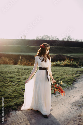 beautiful bride in a light dress and a bouquet on the background of the setting sun on nature. flowers in hair