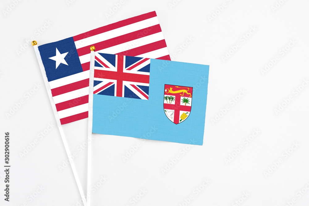 Fototapeta premium Fiji and Liberia stick flags on white background. High quality fabric, miniature national flag. Peaceful global concept.White floor for copy space.