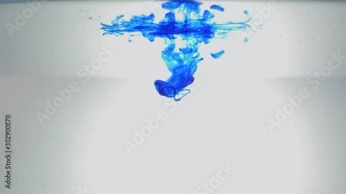 Blue inkdrop moving in water on white background. Acrylic ink swirling in water. Abstract clouds of paint. Against white background. With water surface. photo