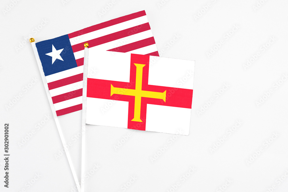 Guernsey and Liberia stick flags on white background. High quality fabric, miniature national flag. Peaceful global concept.White floor for copy space.