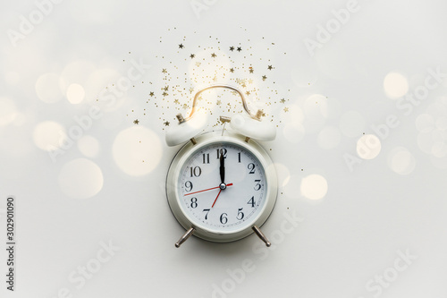 Flat lay composition with alarm clock and golden stars confetti on white background