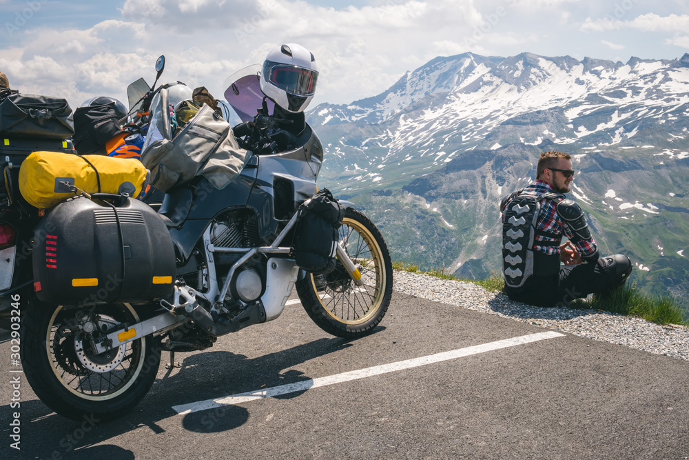 Fototapeta Motocyklista siedzący na skraju ziemi i spoglądający w dal. szczyt góry, przełęcz Grossglockner, rowerzysta ubrany w zbroję ochronną. Austria, motocykl z torbami