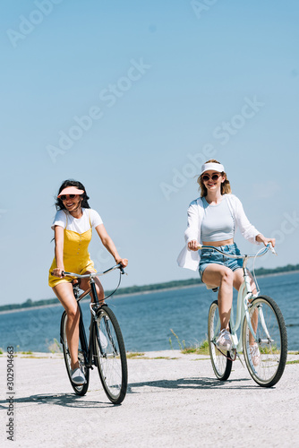 smiling blonde and brunette girls riding bikes near river in summer © LIGHTFIELD STUDIOS