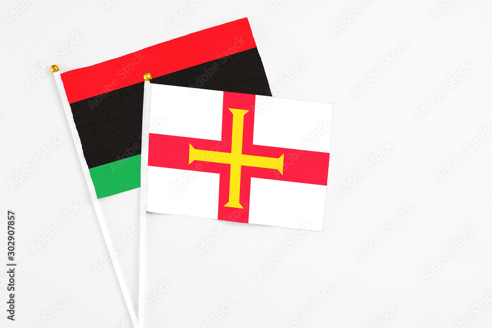 Guernsey and Libya stick flags on white background. High quality fabric, miniature national flag. Peaceful global concept.White floor for copy space.