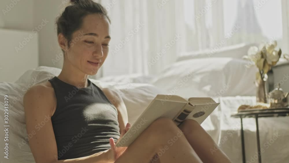 Satisfied pretty asian woman reading book while sitting on the floor at home Satisfied pretty asian woman reading book while sitting on the floor at home