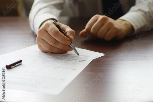 Business meeting. A man signs a contract. Male hand with pen makes notes in the office.