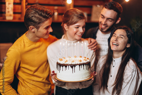Surprise for her. Group of happy people celebrating birthday party with friends and smiling during party. Smiling attractive girl holding a cake in her hands