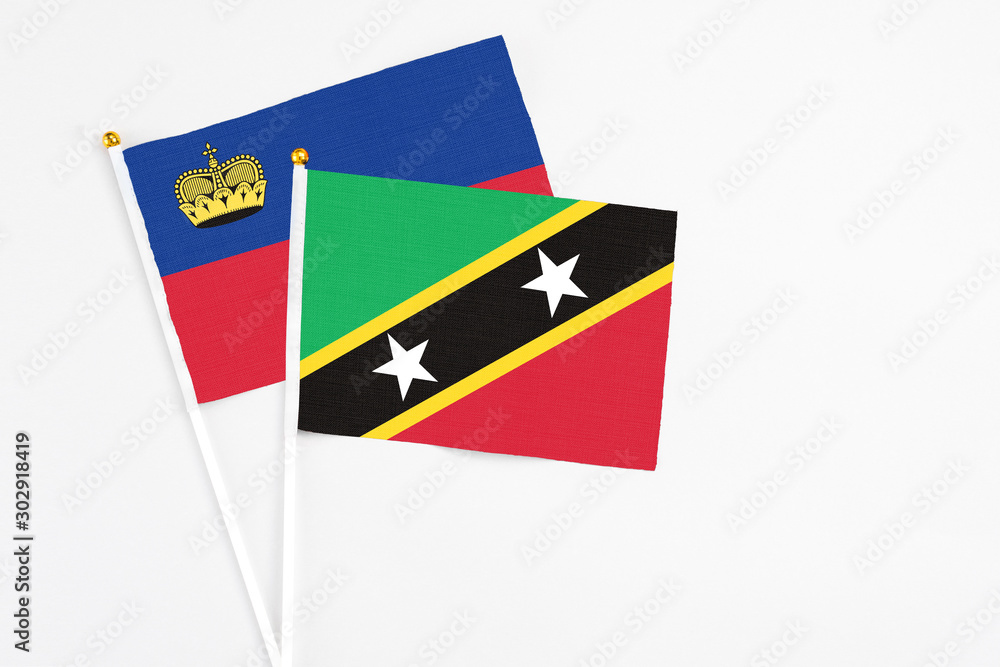 Obraz premium Saint Kitts And Nevis and Liechtenstein stick flags on white background. High quality fabric, miniature national flag. Peaceful global concept.White floor for copy space.