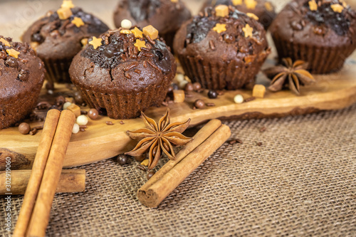 Chocolate holiday cupcakes, muffins with cake sprinkles on a wooden board, chocolate, cinnamon sticks, star anise, burlap sack