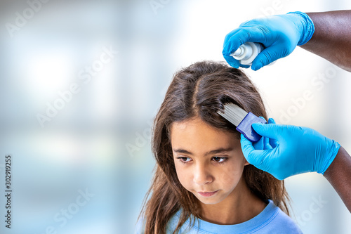 Mother treating daughter's hair against lice ith spray treament photo